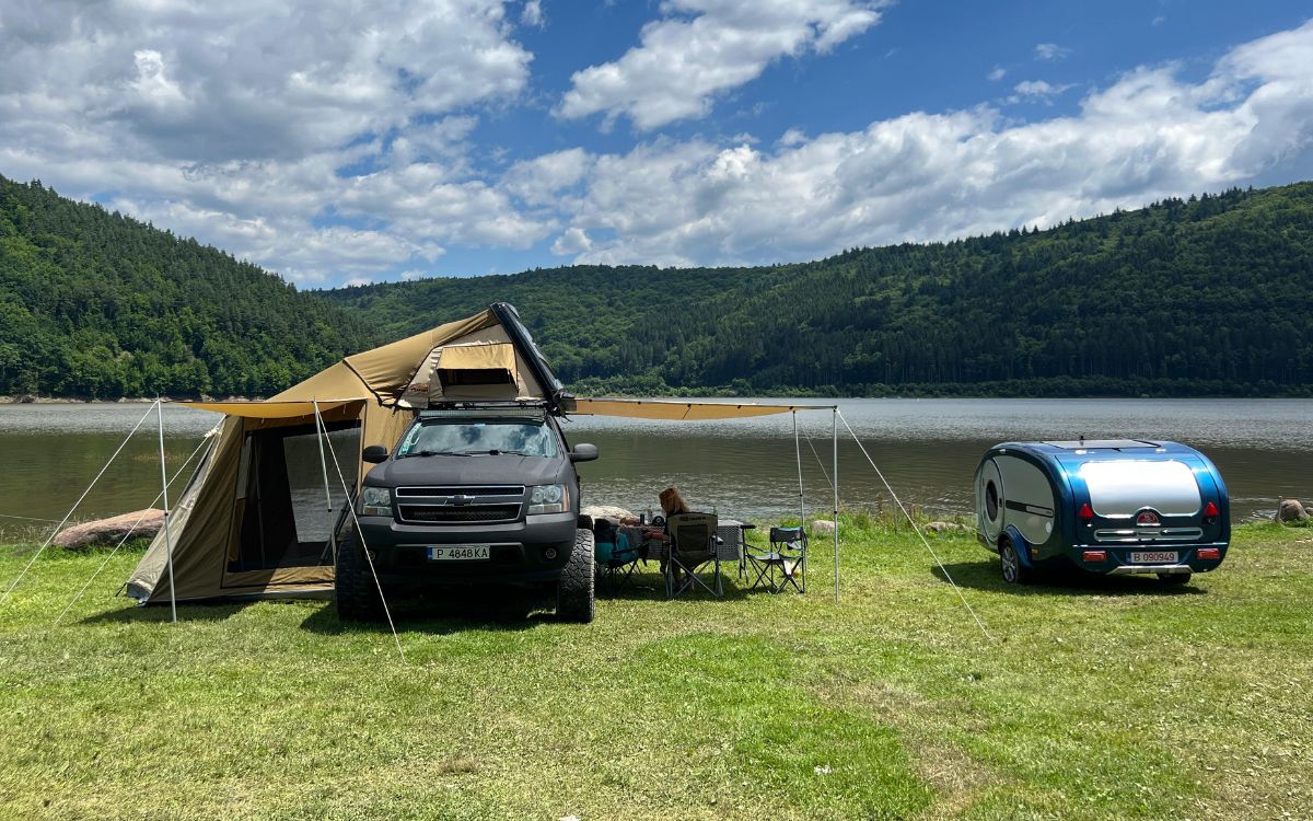 Mașină echipată cu cort de plafon și minirulotă, la camping lângă un lac de munte